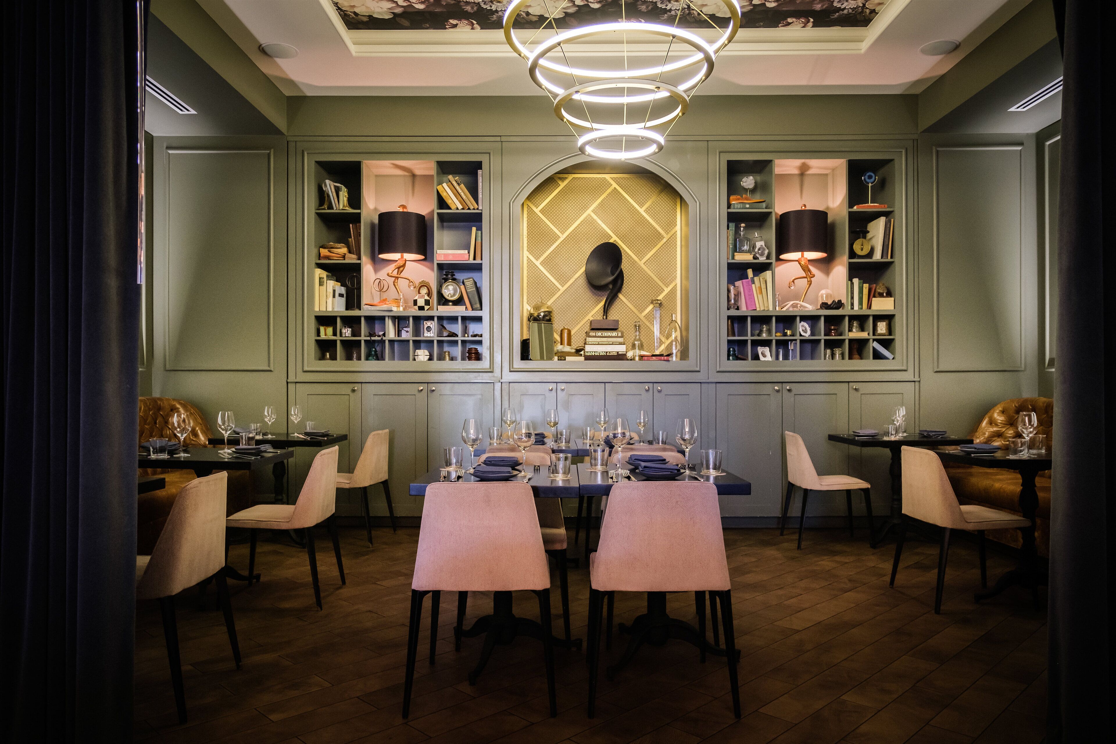 A dining area with a long table set for six, flanked by bookshelves and a decorative ceiling light.
