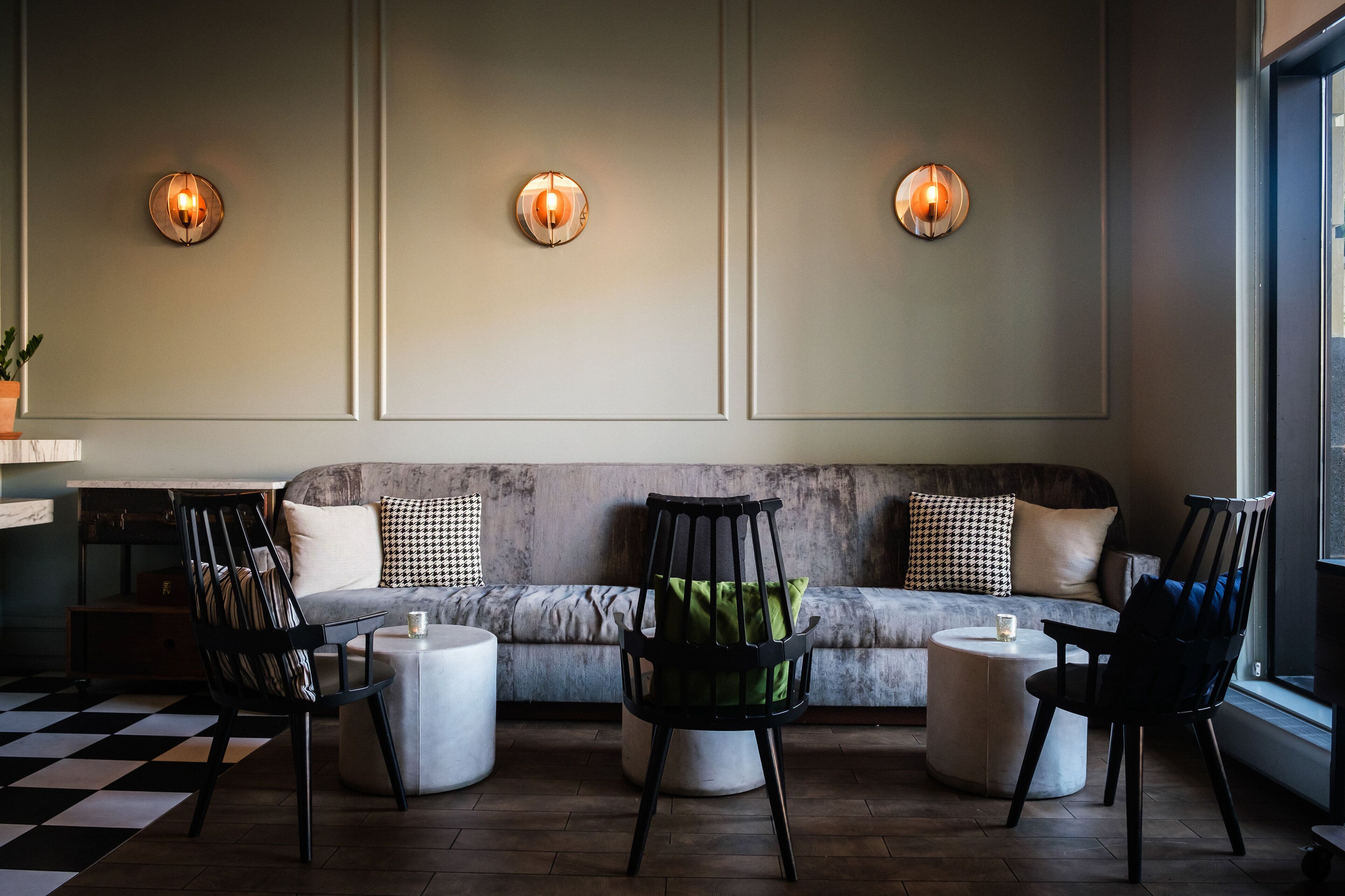 Un área de descanso moderna con un sofá, dos sillones, una mesita y luces fijadas a la pared.