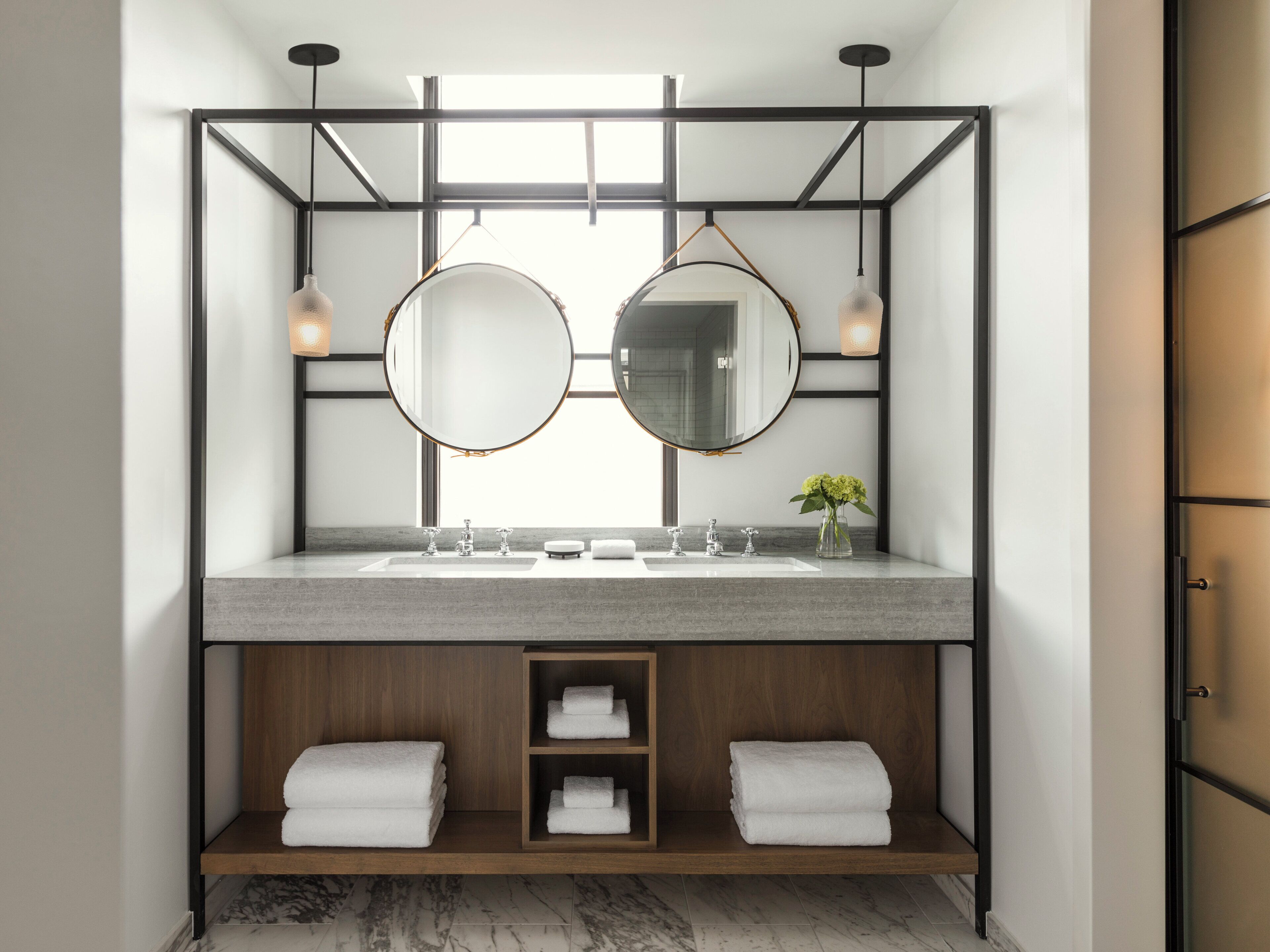Een moderne badkamer met een dubbele wastafel, twee ronde spiegels en een houten plank met handdoeken.