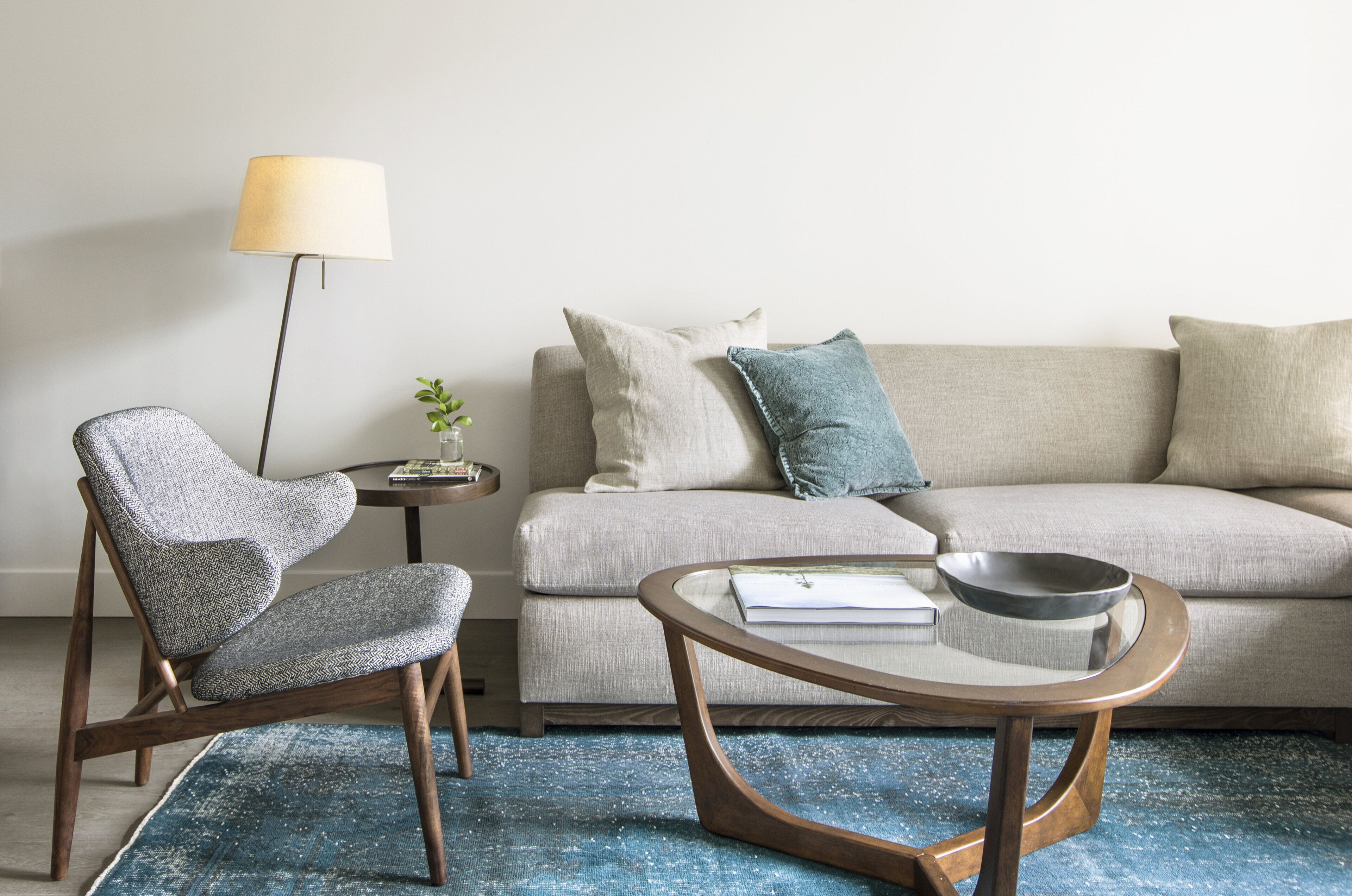 Una sala de estar moderna con un sofá gris, un sillón estampado, una mesa de centro redonda y una lámpara de pie.