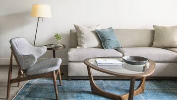 Una sala de estar moderna con un sofá gris, un sillón estampado, una mesa de centro redonda y una lámpara de pie.