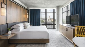A modern hotel room with a large bed, a TV, a desk, and a view of the city. - Kimpton Aertson Hotel by IHG (Nashville)