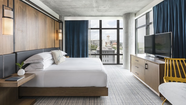 Una habitación de hotel moderna con una cama grande, televisión, escritorio y vistas a la ciudad.