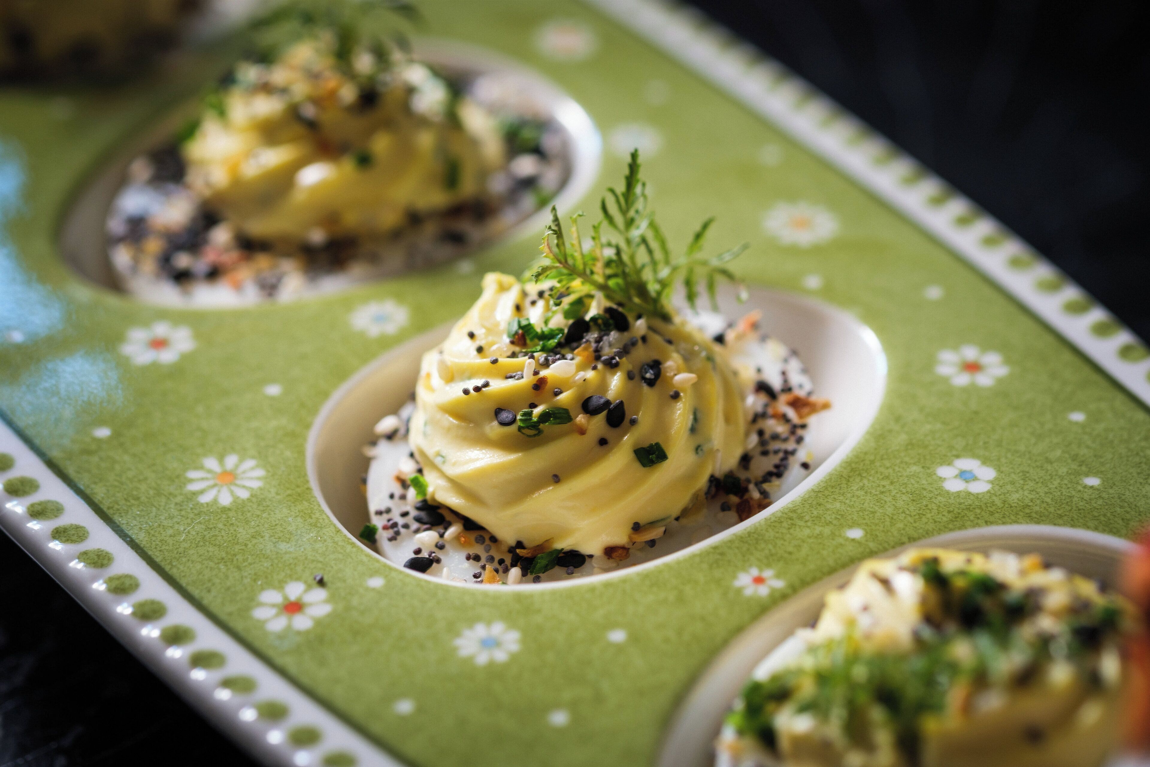 A plate with a creamy dish garnished with herbs and seeds, served on a green floral-patterned plate.