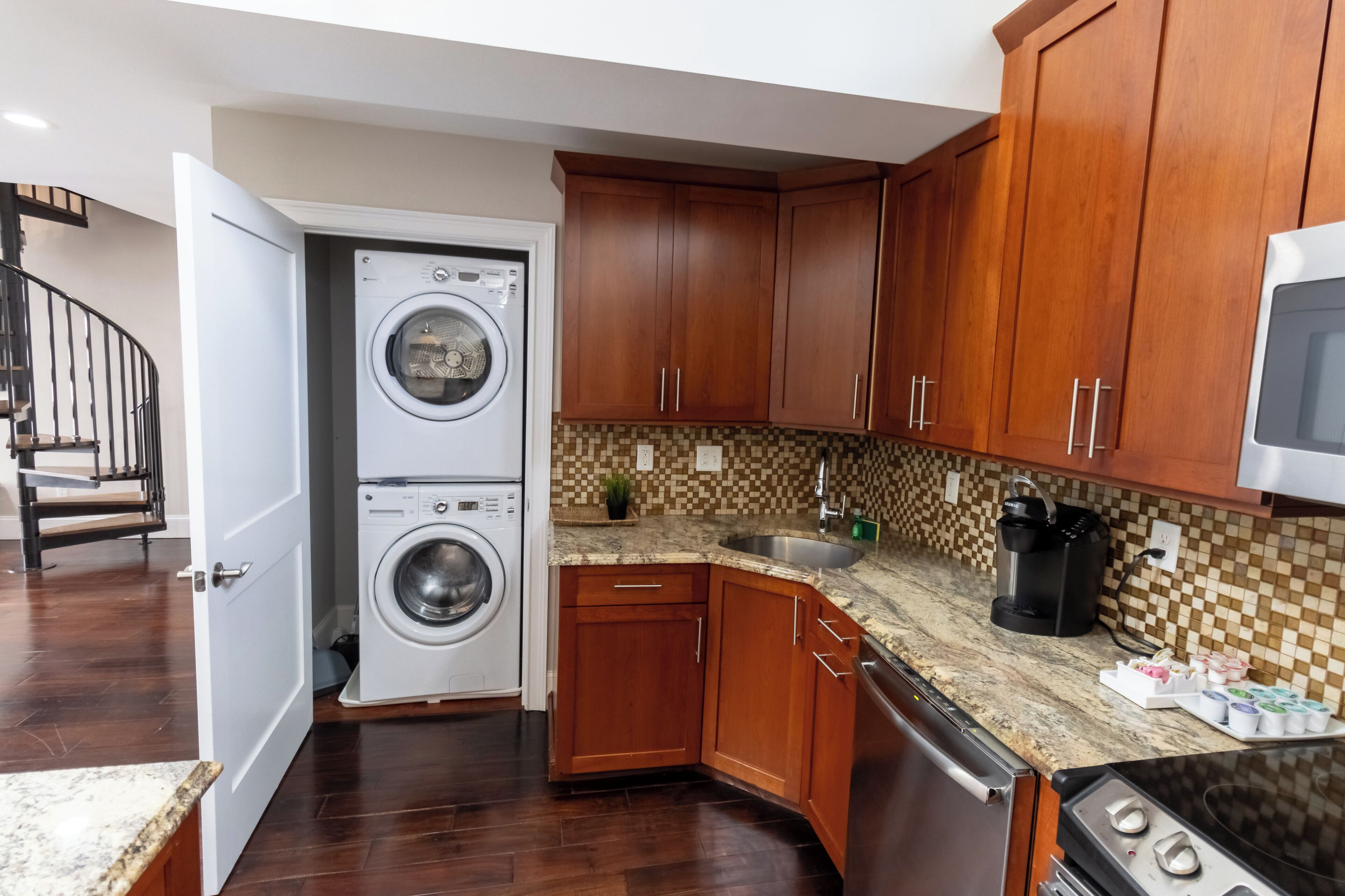 A compact kitchen with wooden cabinets, a built-in washing machine, a microwave, and a granite countertop.