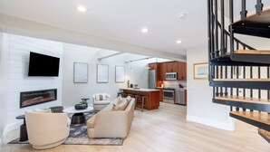 A spacious living area with a fireplace, a sofa, a coffee table, and a TV mounted on the wall. - The Newport Lofts – 543 Thames Street (Newport)