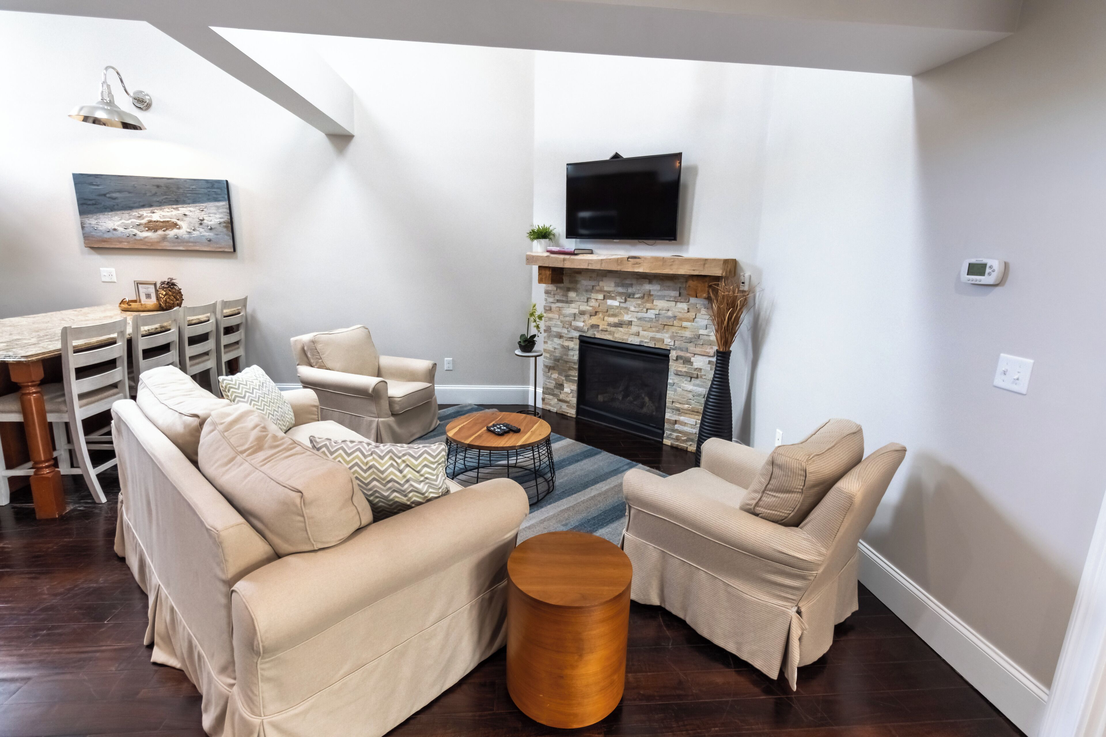 A modern living room with a fireplace, beige sofas, a coffee table, and a dining area with a wooden table and chairs.