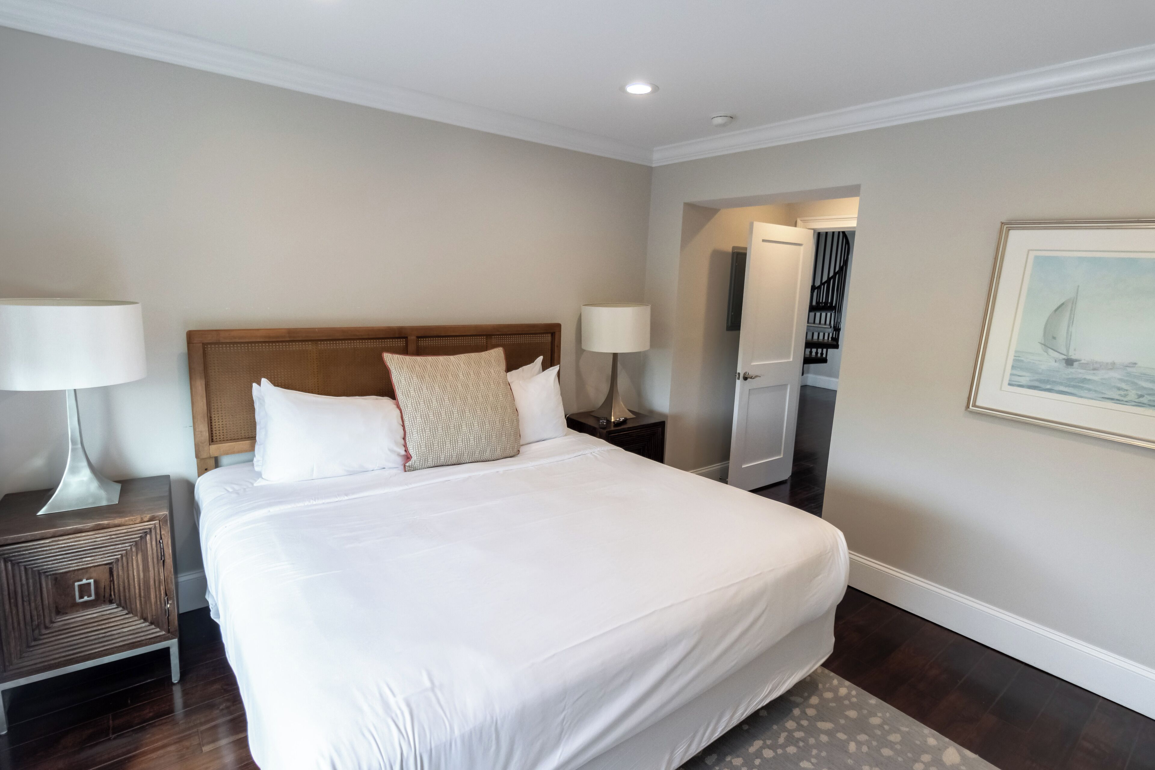 A neatly made bed with white linens and a wooden headboard, flanked by two bedside tables with lamps.