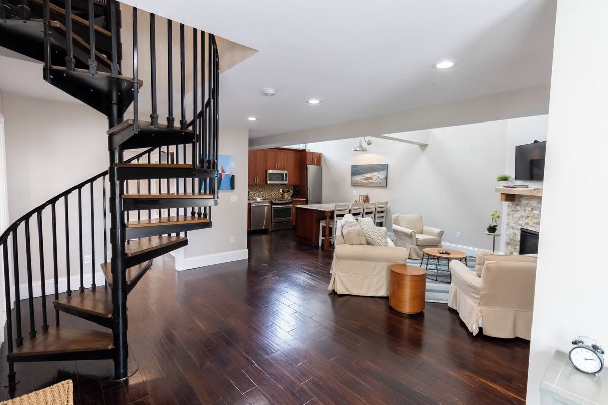 Un vaste espace de vie agrémenté d’un escalier en bois, une cuisine à l’arrière-plan et un coin salon avec une table basse.
