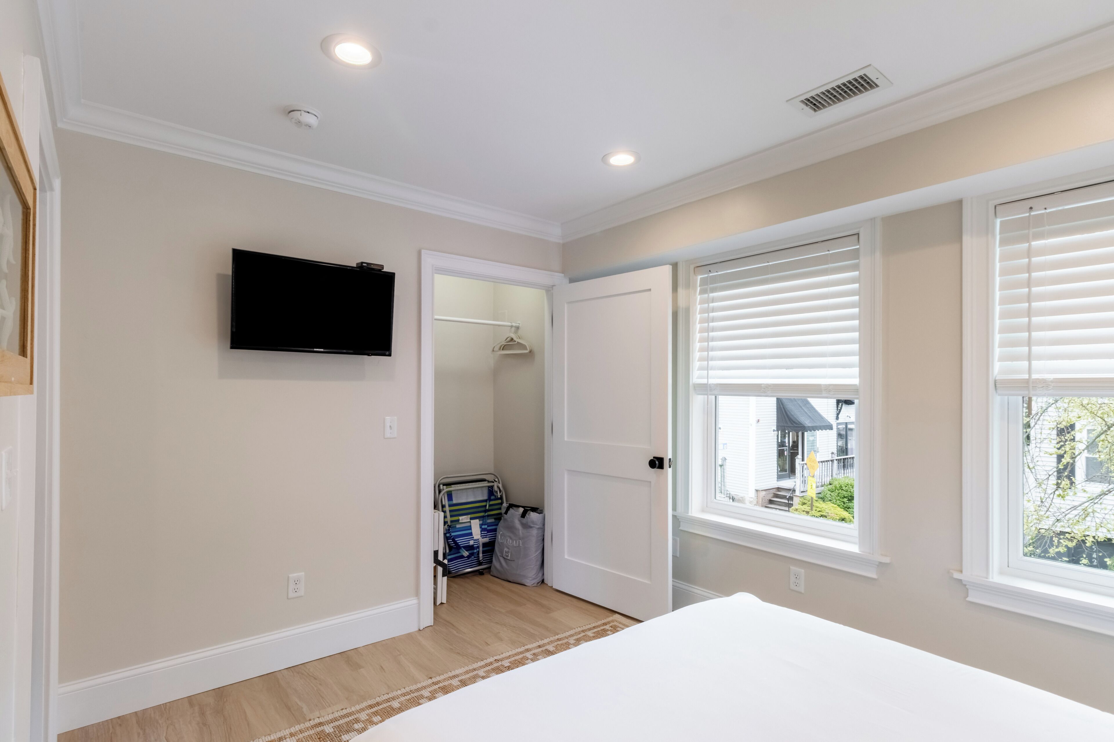 A bedroom with a large window, a flat-screen TV mounted on the wall, and a door leading to a closet.