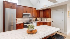 A modern kitchen with wooden cabinets, stainless steel appliances, a marble countertop, and a central island with a plant. - The Newport Lofts – 543 Thames Street (Newport)