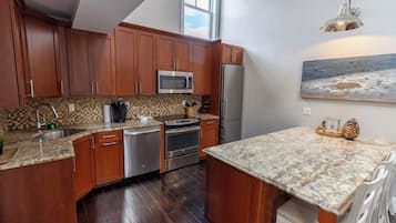 A kitchen with wooden cabinets, stainless steel appliances, a granite countertop, and a dining area with white chairs.