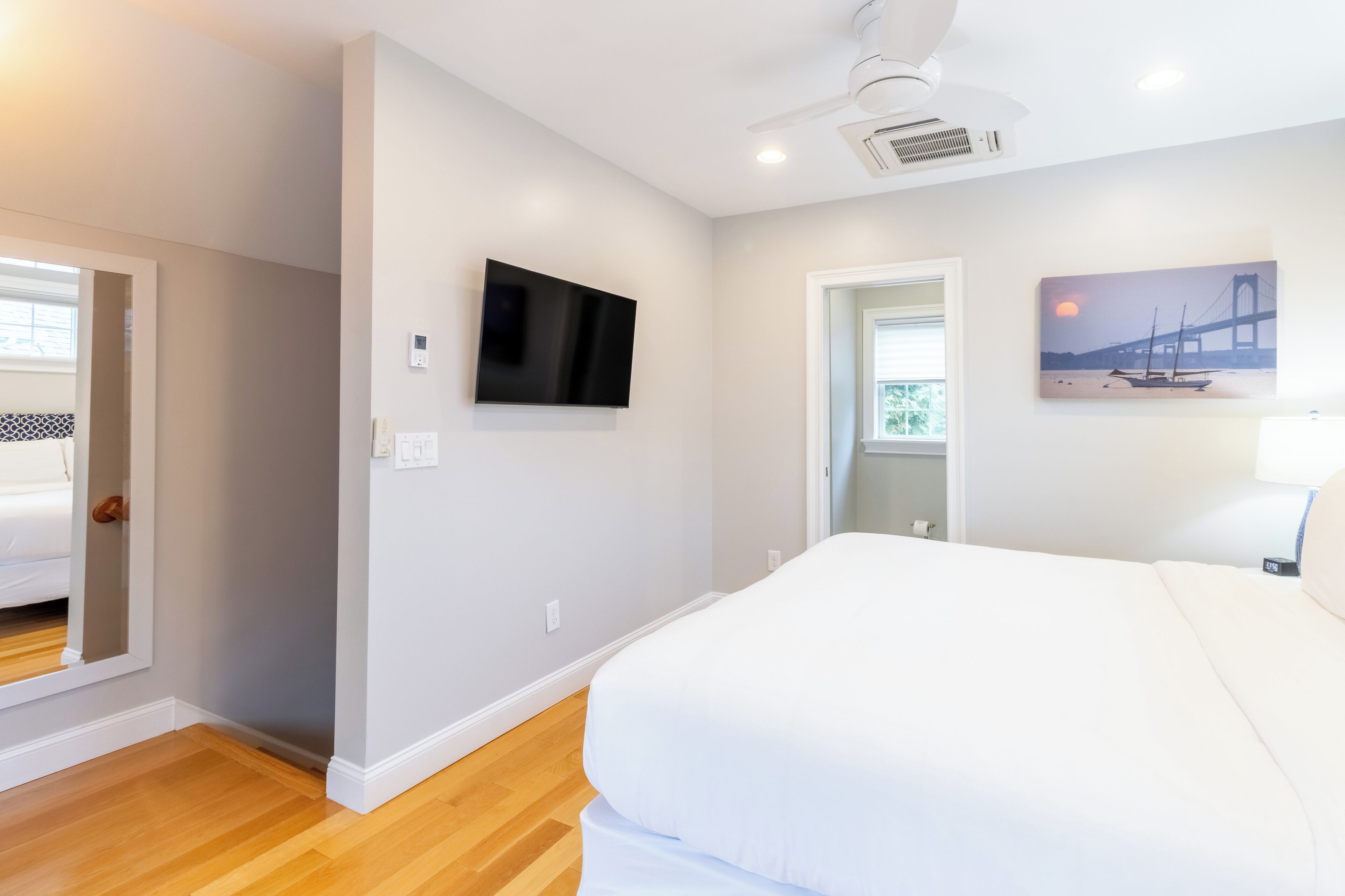Een slaapkamer met een groot bed, een flatscreen-tv aan de muur en een schilderij van een brug.