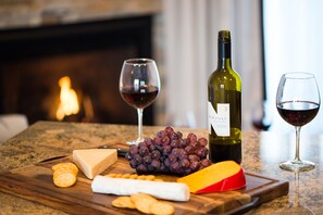 Une planche en bois garnie de fromage, de raisins, de crackers et d’une bouteille de vin, posée sur un comptoir de cuisine.
