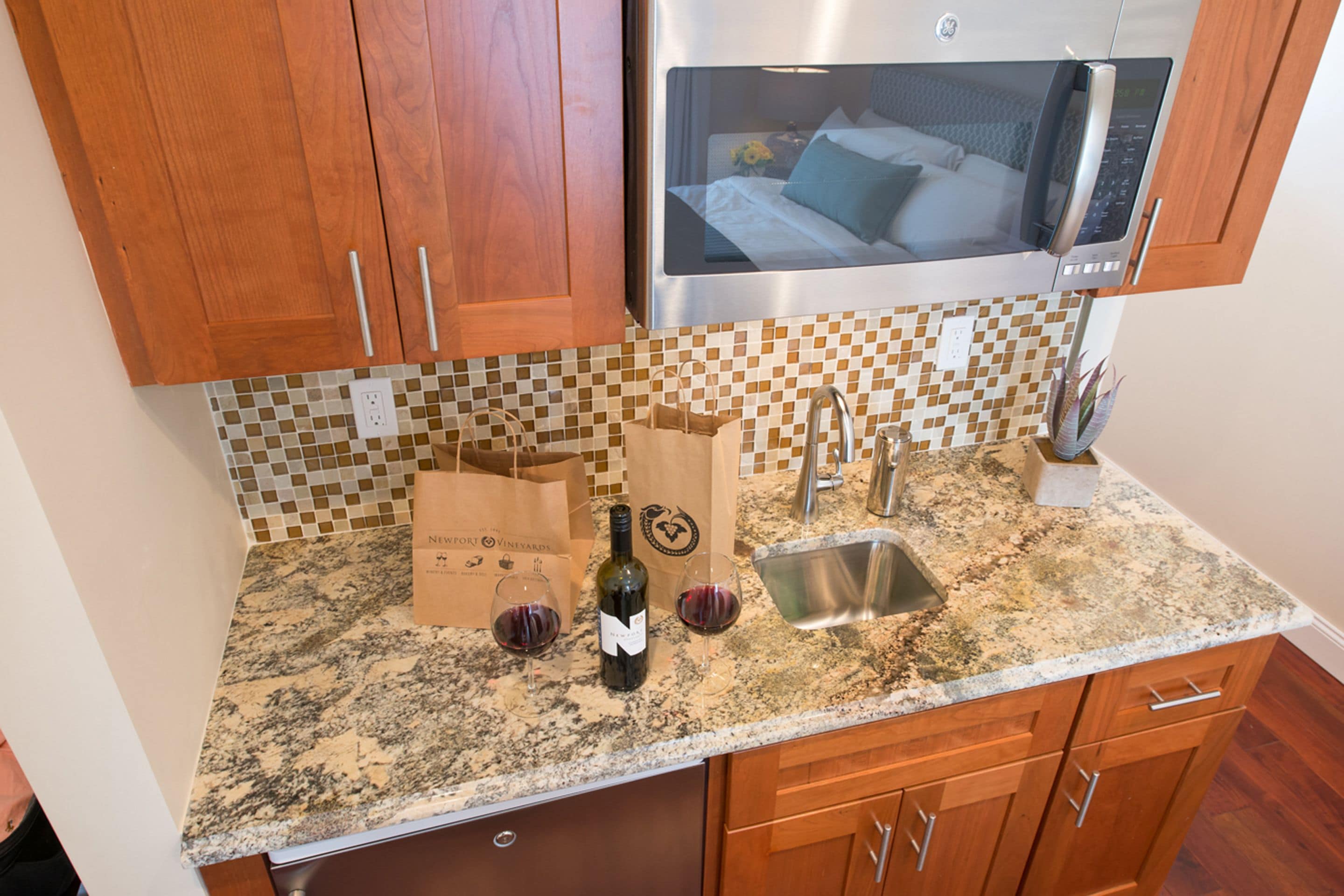 A kitchen with wooden cabinets, a stainless steel microwave, a granite countertop, a sink, and wine glasses.