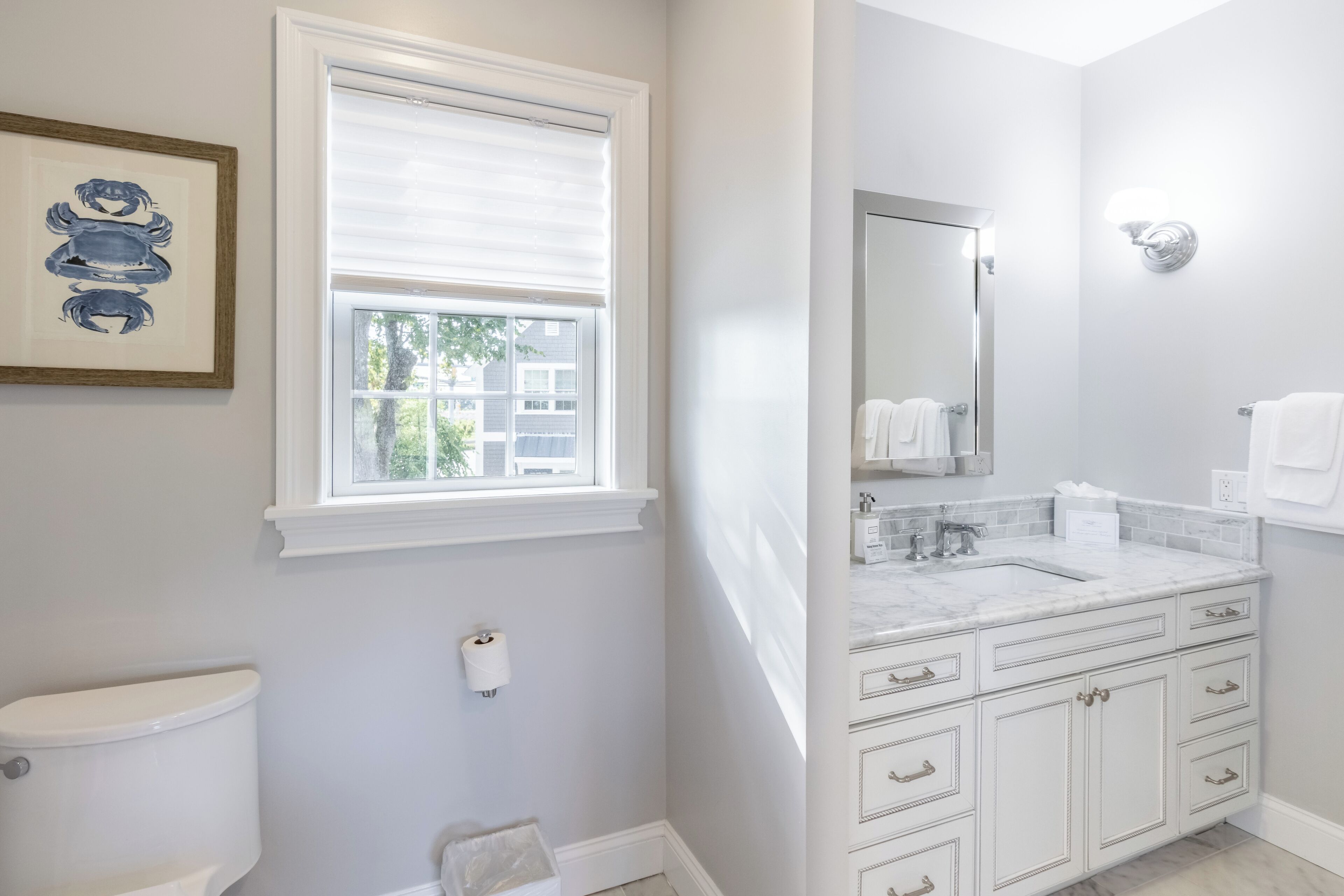 A bathroom with a toilet, a window, a sink with a mirror, and a towel rack.