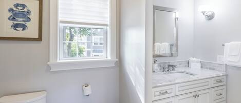 A bathroom with a toilet, a window, a sink with a mirror, and a towel rack.