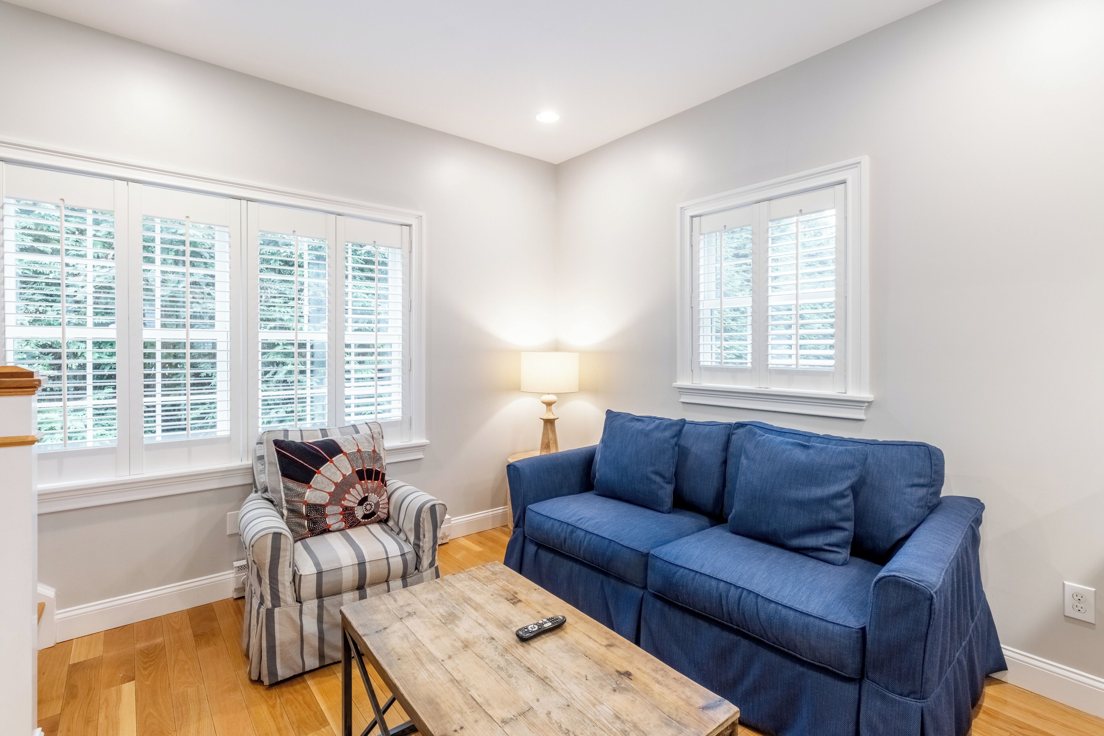 A living room with a blue sofa, a plaid armchair, a wooden coffee table, and a lamp.