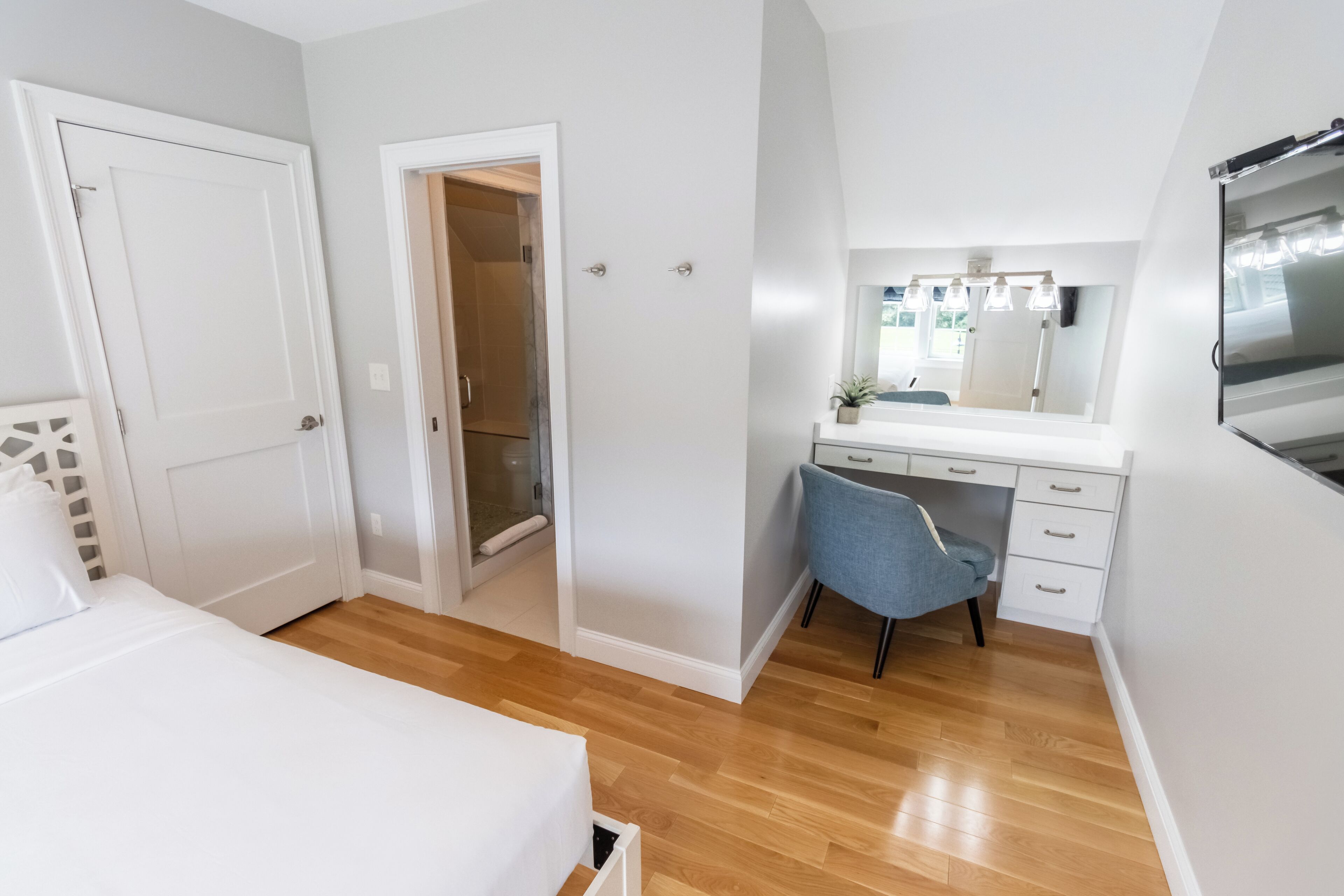A bedroom with a bed, a desk, a chair, a mirror, and a wardrobe.