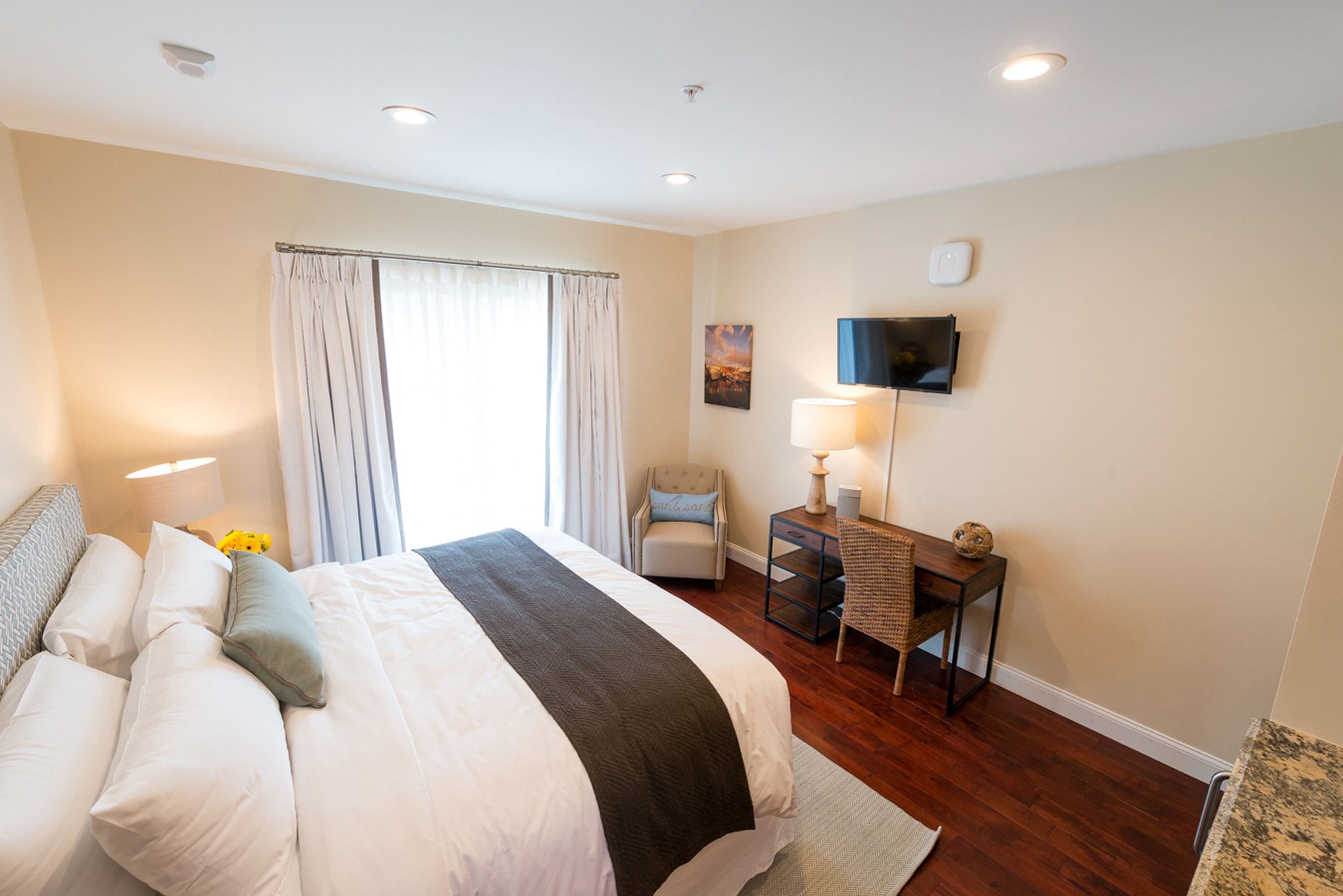 A hotel room with a large bed, a desk, a chair, a flat-screen TV, and a window with curtains.