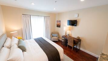 A hotel room with a large bed, a desk, a chair, a flat-screen TV, and a window with curtains.