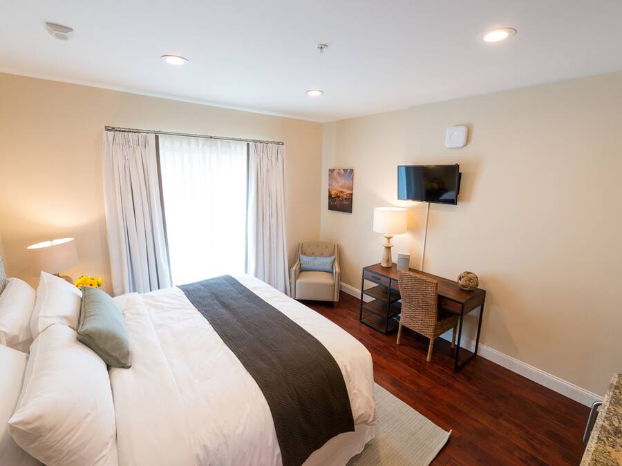 A hotel room with a large bed, a desk, a chair, a flat-screen TV, and a window with curtains.
