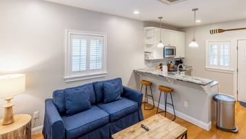 A compact living space with a blue sofa, wooden coffee table, and a kitchen area with white cabinets and a marble countertop.