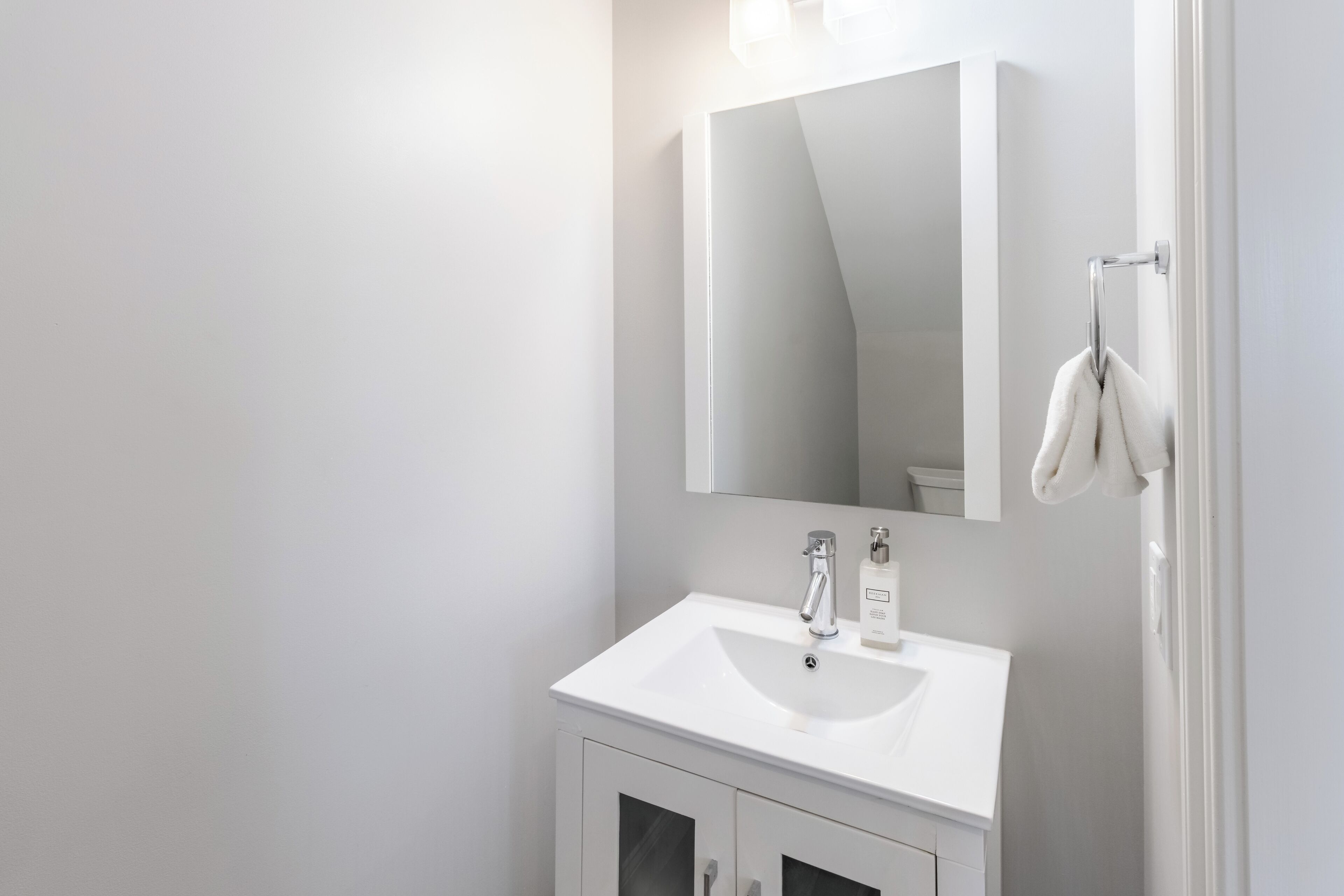 A modern bathroom with a white sink, a mirror, and a towel rack.