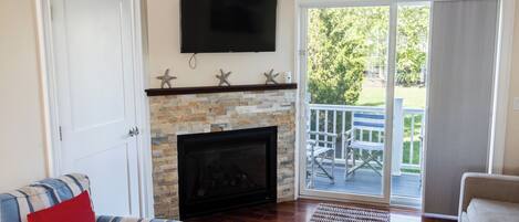 A living room with a fireplace, a television mounted above it, and a sliding glass door leading to an outdoor deck.