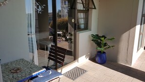 A glass door leading to a patio with a table and a bench, a potted plant, and a view of the outside.