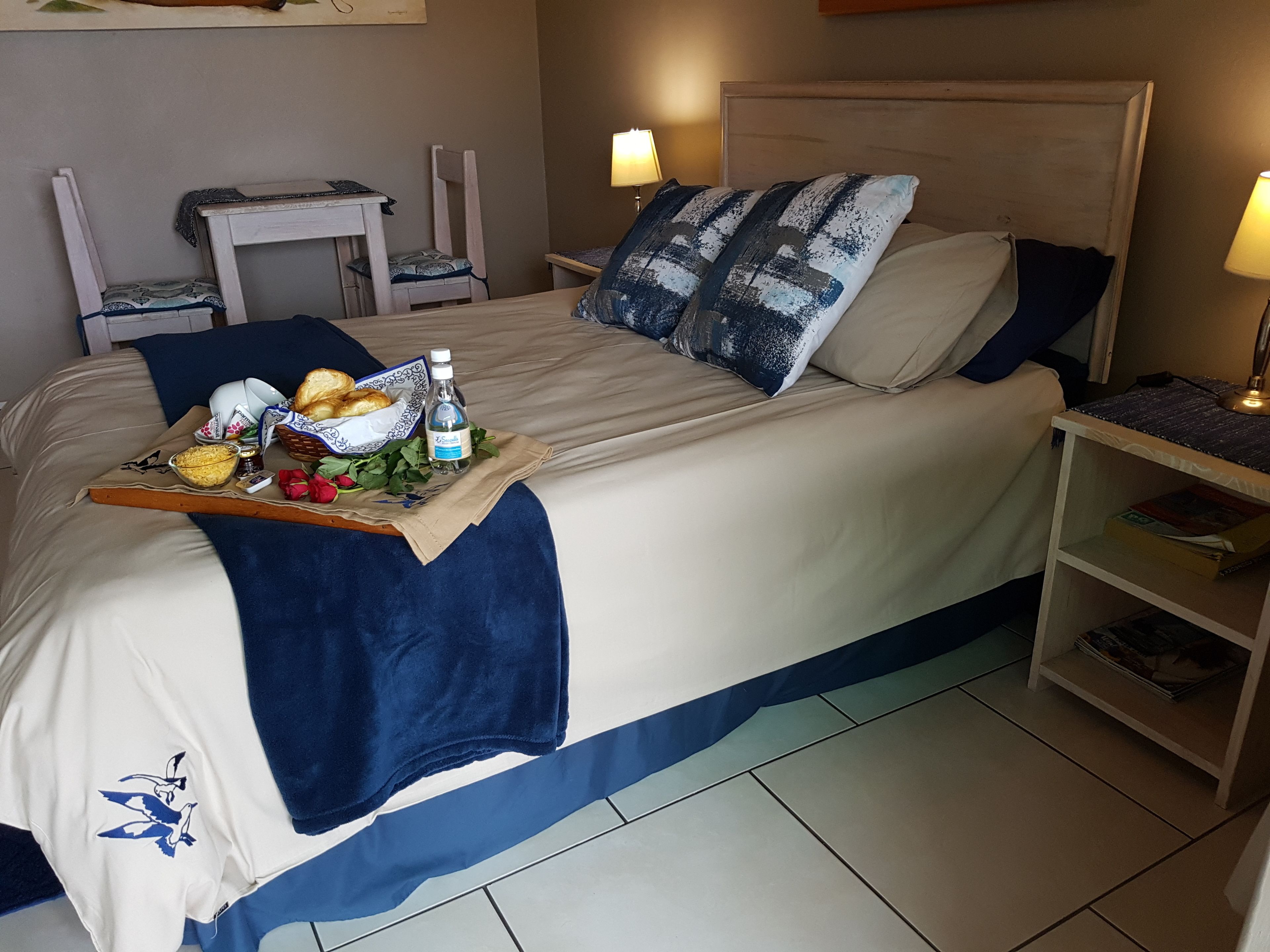 Ein ordentlich bezogenes Bett mit einem Frühstücksbrettchen, einem Nachttisch mit Lampe und einem Stuhl.