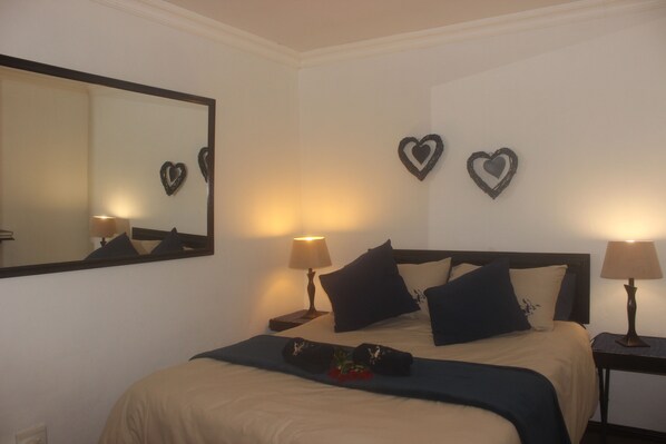 A neatly made bed with a beige and dark blue bedspread, two heart-shaped wall decorations, and two bedside lamps.
