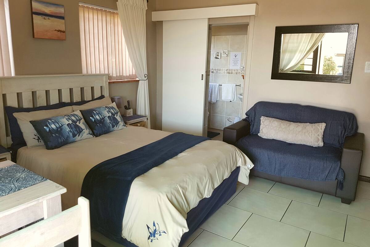 A bedroom with a bed, a sofa, a small table, and a bathroom visible through an open door.