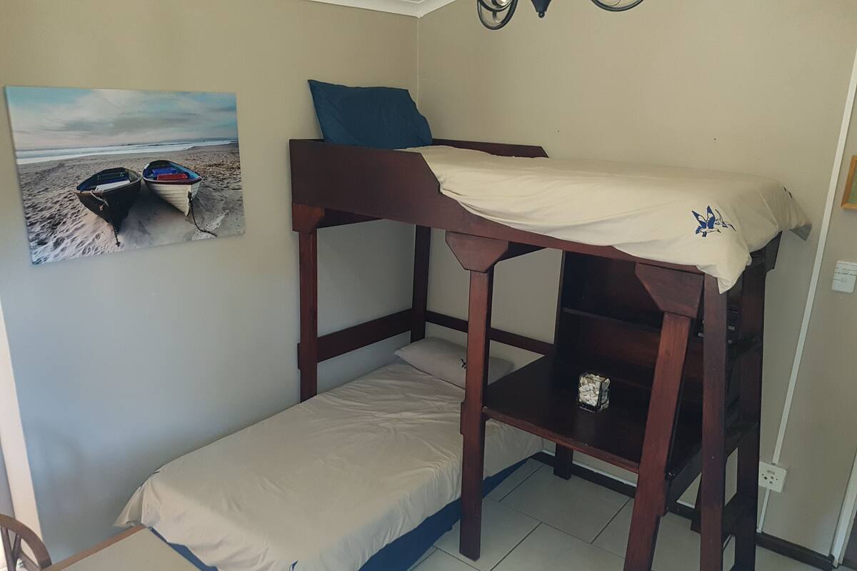 A bunk bed with a lower bunk and a small shelf below. There is a picture of boats on the wall to the left.