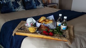 A neatly made bed with a tray of breakfast items including croissants, a bowl of cereal, and two bottles of water.