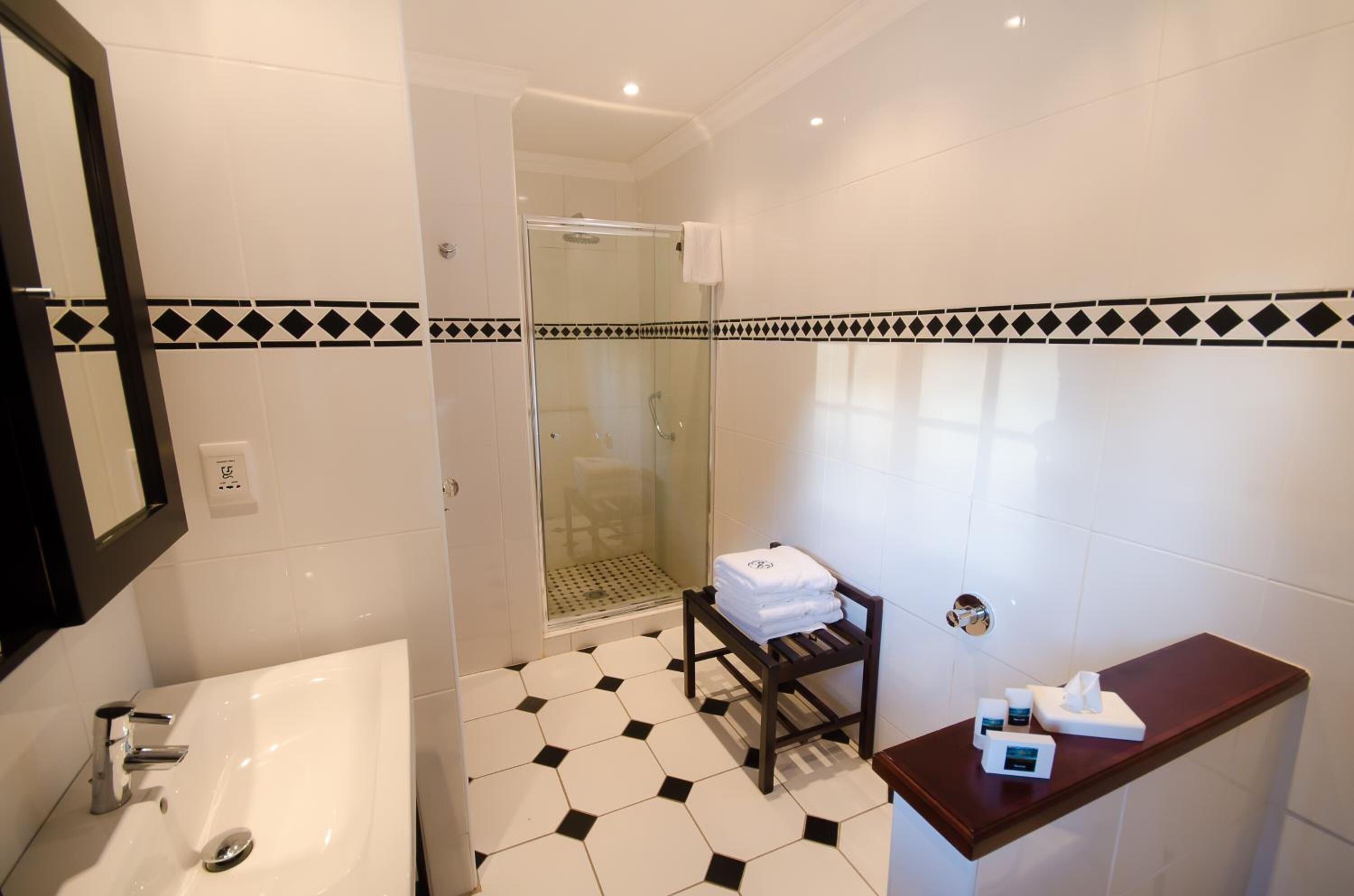 Een badkamer met een witte wasbak, een douchecabine van glas en een houten plank met toiletartikelen.