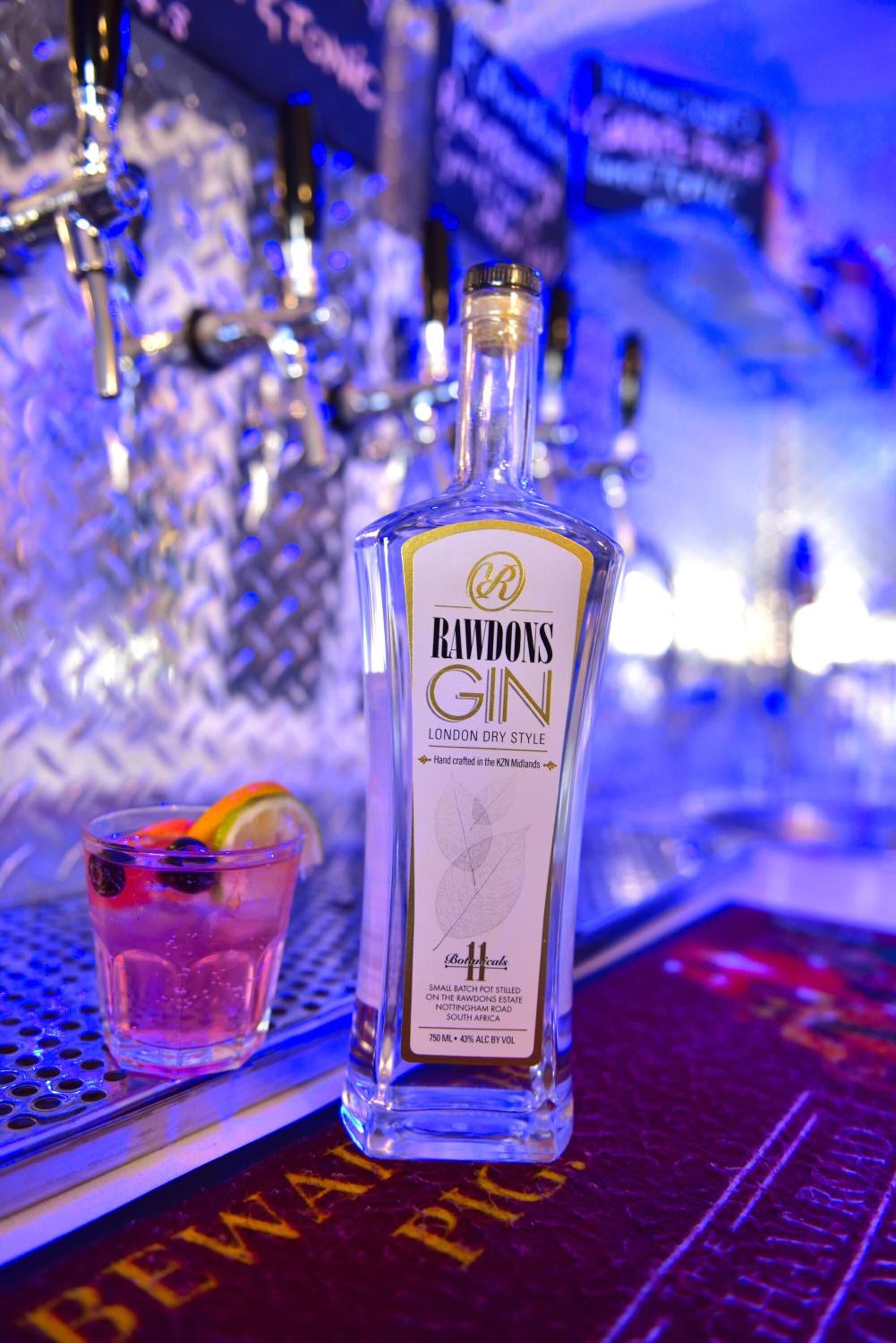 A bottle of Raudons Gin and a glass with a slice of lime on a bar counter.