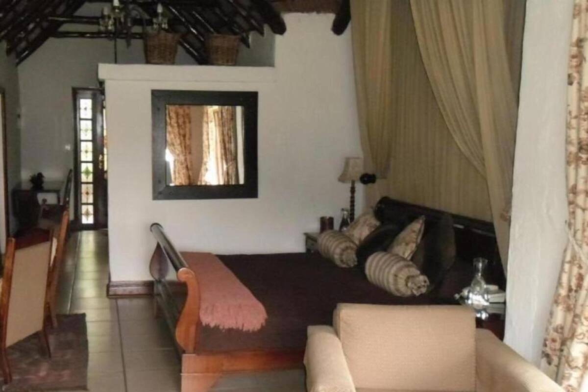 Quarto com uma cama, um sofá, uma mesa pequena com abajur e uma janela com cortinas.