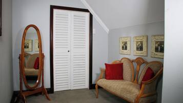 Una habitación con una silla de madera, un espejo, una puerta blanca y tres cuadros en la pared.