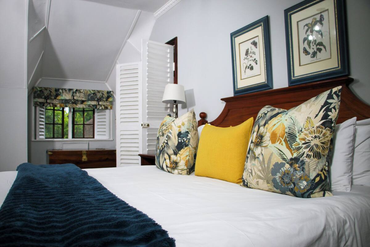 Quarto com cama, luminária e dois quadros de ilustrações botânicas na parede.