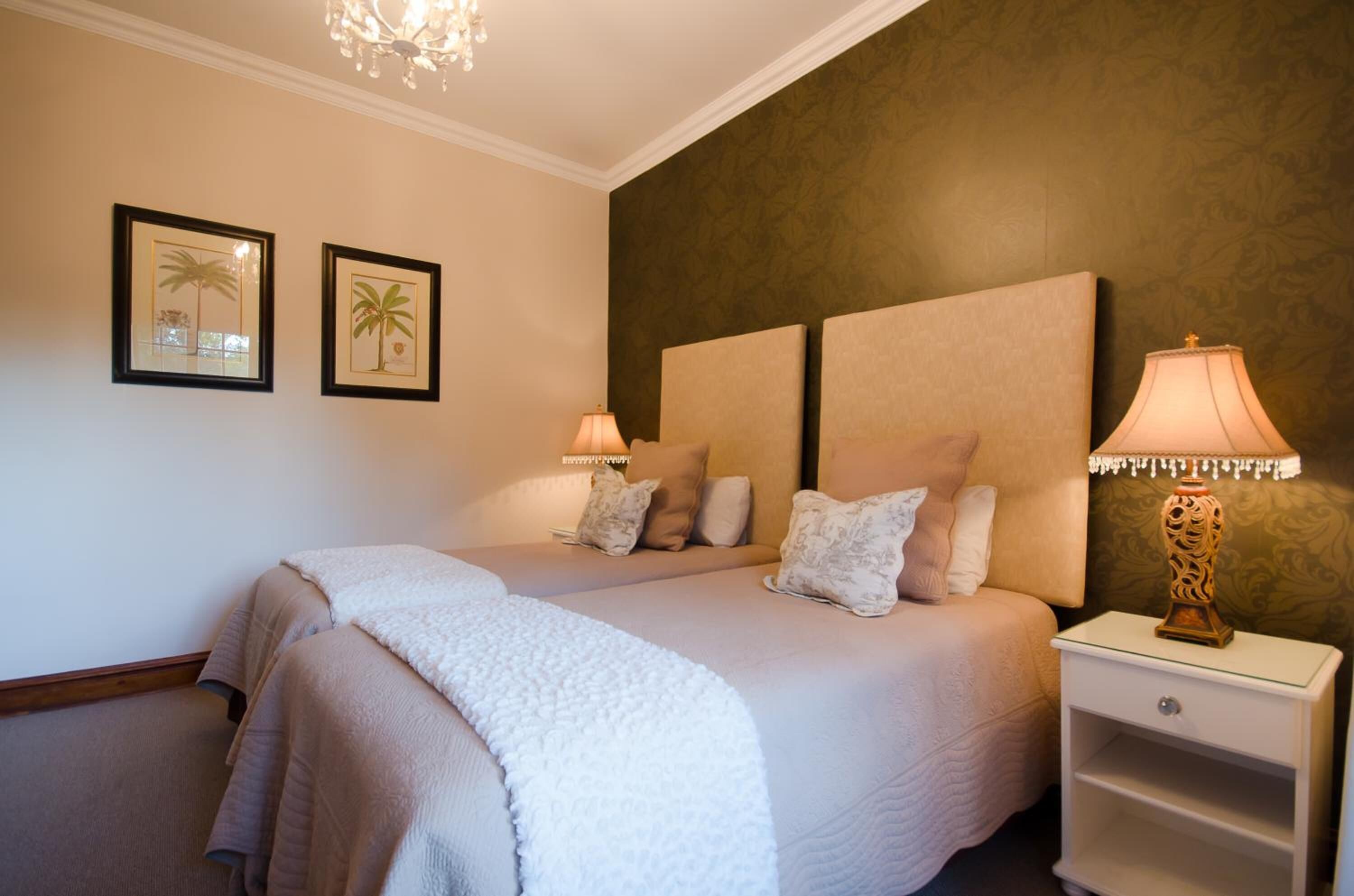 A double bed with two nightstands, each with a lamp, in a room with a patterned wall and framed pictures.