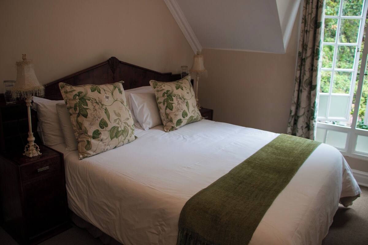 Uma cama bem arrumada com almofadas florais, um cobertor verde e uma mesinha de cabeceira com abajur.