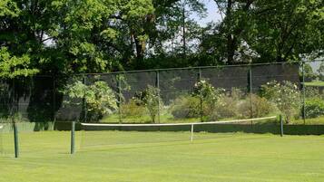 A tennis court with a net, surrounded by a fence and trees.