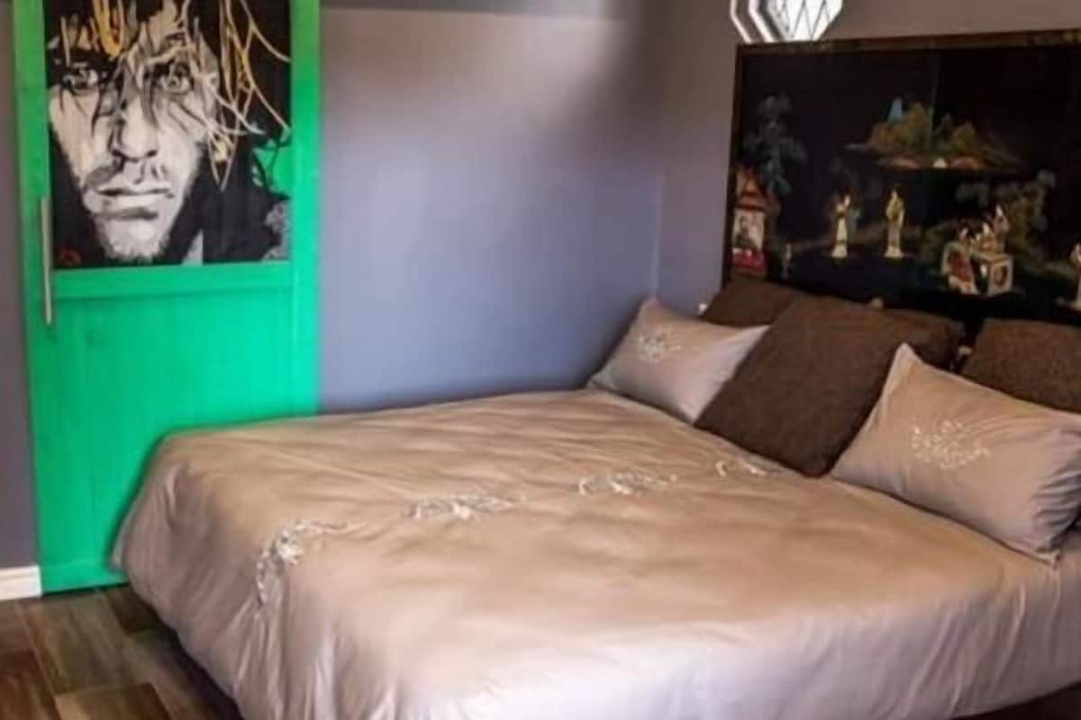 A bedroom with a bed, pillows, a painting, and a green door.