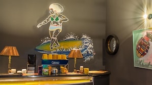 A hotel reception area with a mural of a woman surfing, a coffee machine, and a Carimali coffee display.