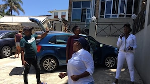 A group of people standing in a parking area with cars and a building in the background.