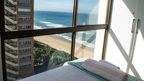 Habitación de hotel con un amplio ventanal con vistas a una playa y al océano.