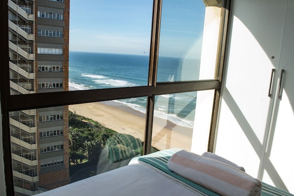 A hotel room with a large window overlooking a beach and ocean.