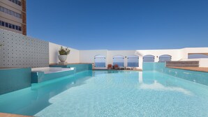 Una piscina con agua azul cristalina, una planta en maceta y vistas al océano a través de ventanas arqueadas.