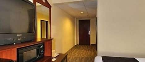 A hotel room with a bed, a television, a microwave, and a mirror.
